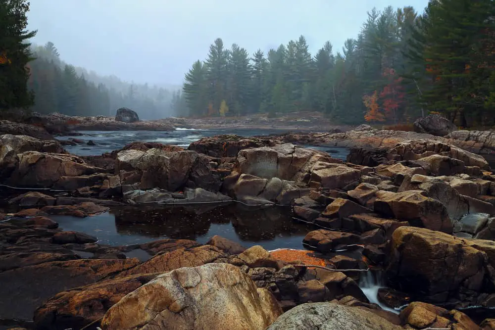 This is a view of the foggy stone river in Quebec with forests around it.