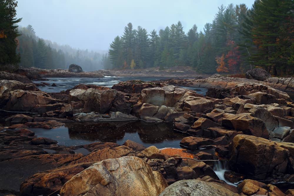 This is a view of the foggy stone river in Quebec with forests around it.