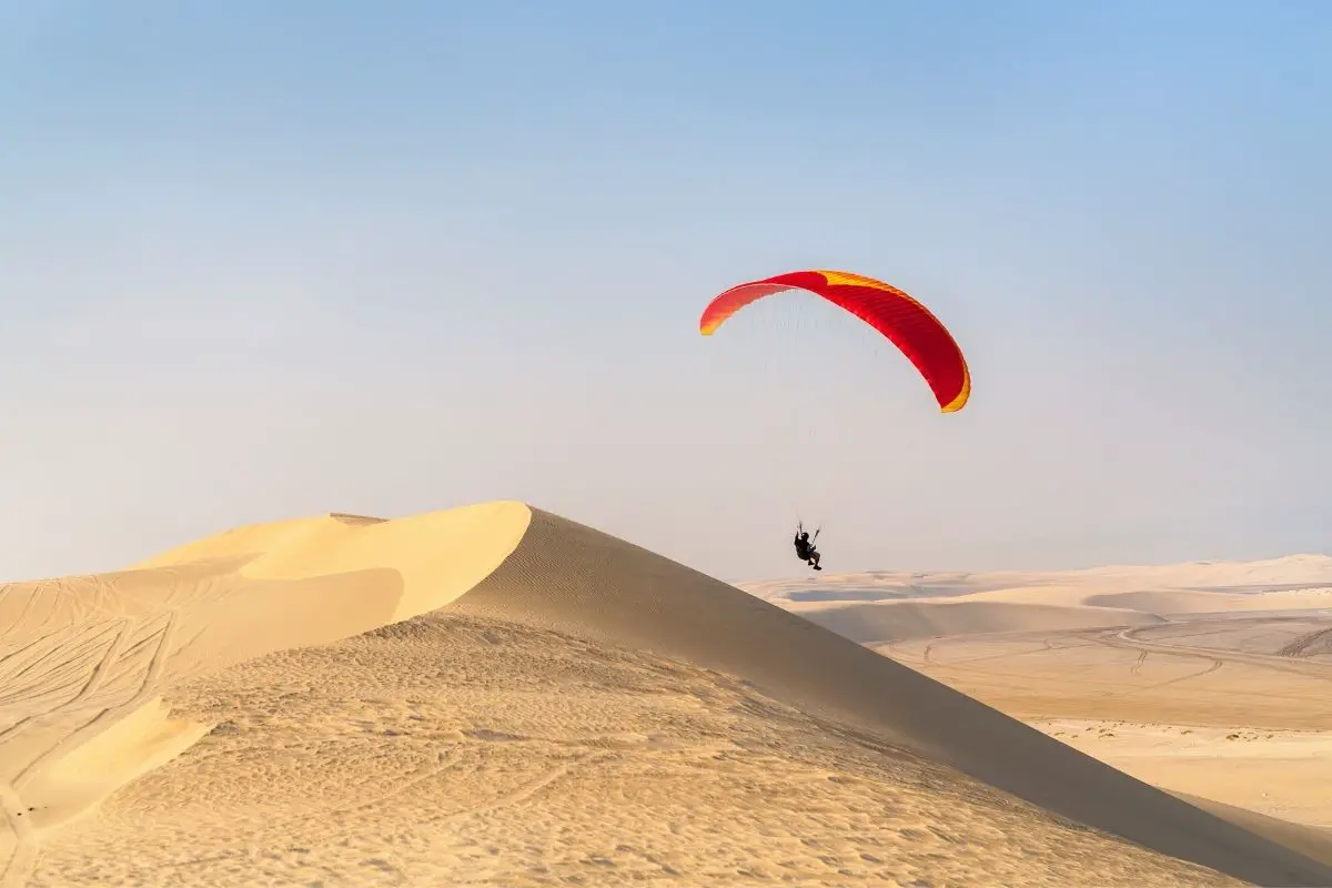 Paraglider flying over sand dunes in qatar.